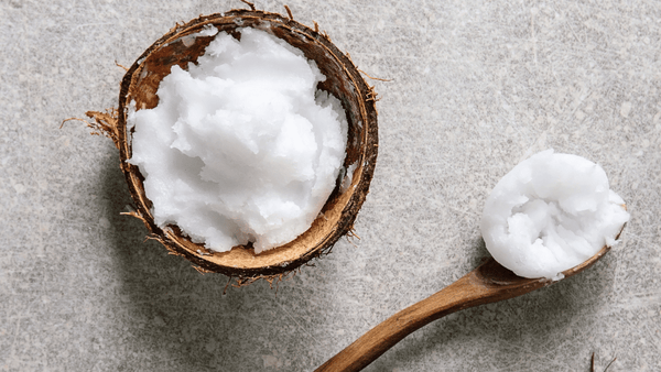Organic coconut oil in a half coconut shell and wooden spoon on a stone surface – natural MCT oil source for keto, skincare, and cooking benefits.