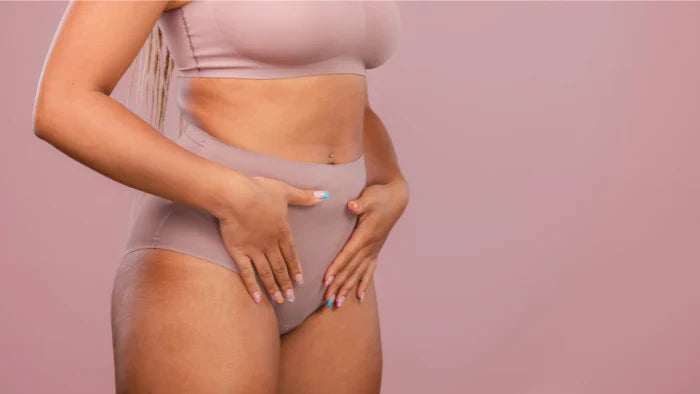Woman in neutral-toned underwear touching her lower abdomen, possibly experiencing bloating or menstrual discomfort. Body positivity and women's health concept.