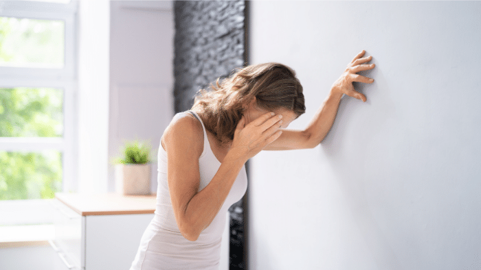 An image of woman feeling dizzy while leaning on the wall