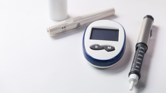 Diabetes management tools, including a blood glucose monitor, insulin pen, and lancet device, placed on a white surface.